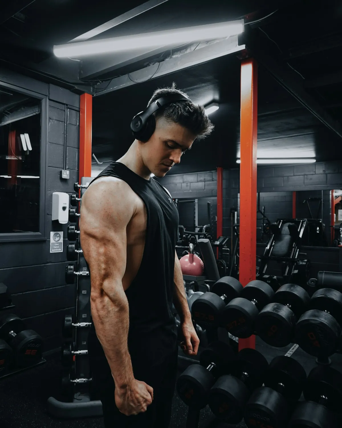Chico con camiseta negra de tirantes entre mancuernas en un gimnasio